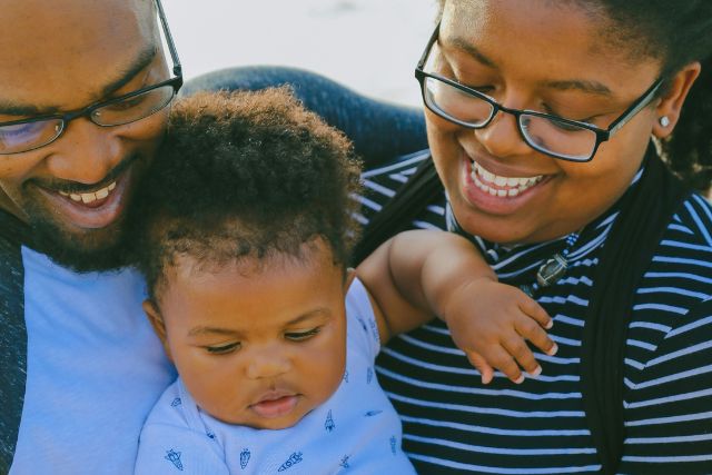 A smiling couple looks down at their young baby with warmth and joy | Pathway Caring for Children
