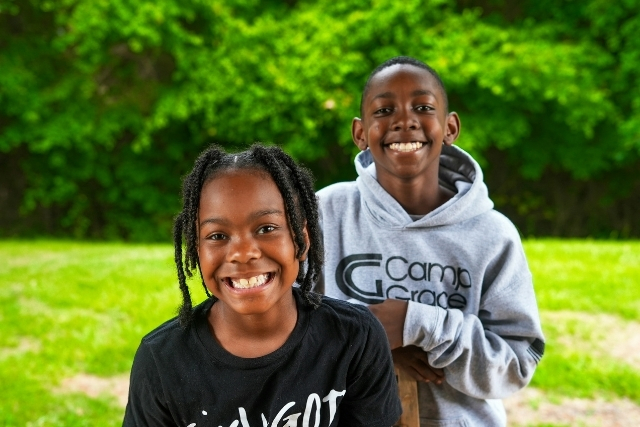 A brother and sister smile together outdoors in front of green trees | Pathway Caring for Children