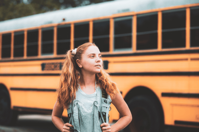 Foster child standing in front of a school bus ready for a new school day and academic success.